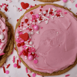 Pink, red, and white sprinkles adorn pink frosted cookie