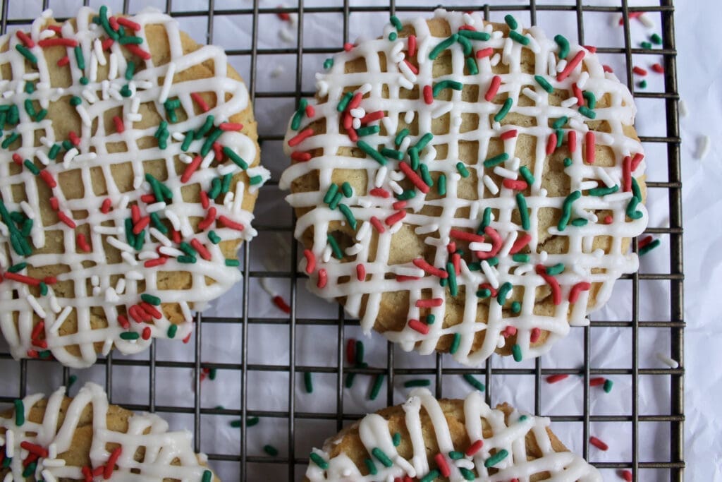 Cookie with Christmas colored sprinkles and white frosting sits on wire cooling wrack