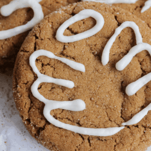 Mint chocolate chip cookies with white frosting drizzle posed on neutral surface.