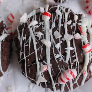 Heavily drizzled dark chocolate cookie sits on parchment paper with chunks of mint spread around.